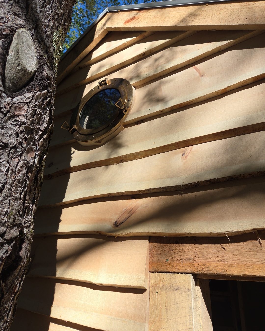 Round porthole window detail on live edge siding